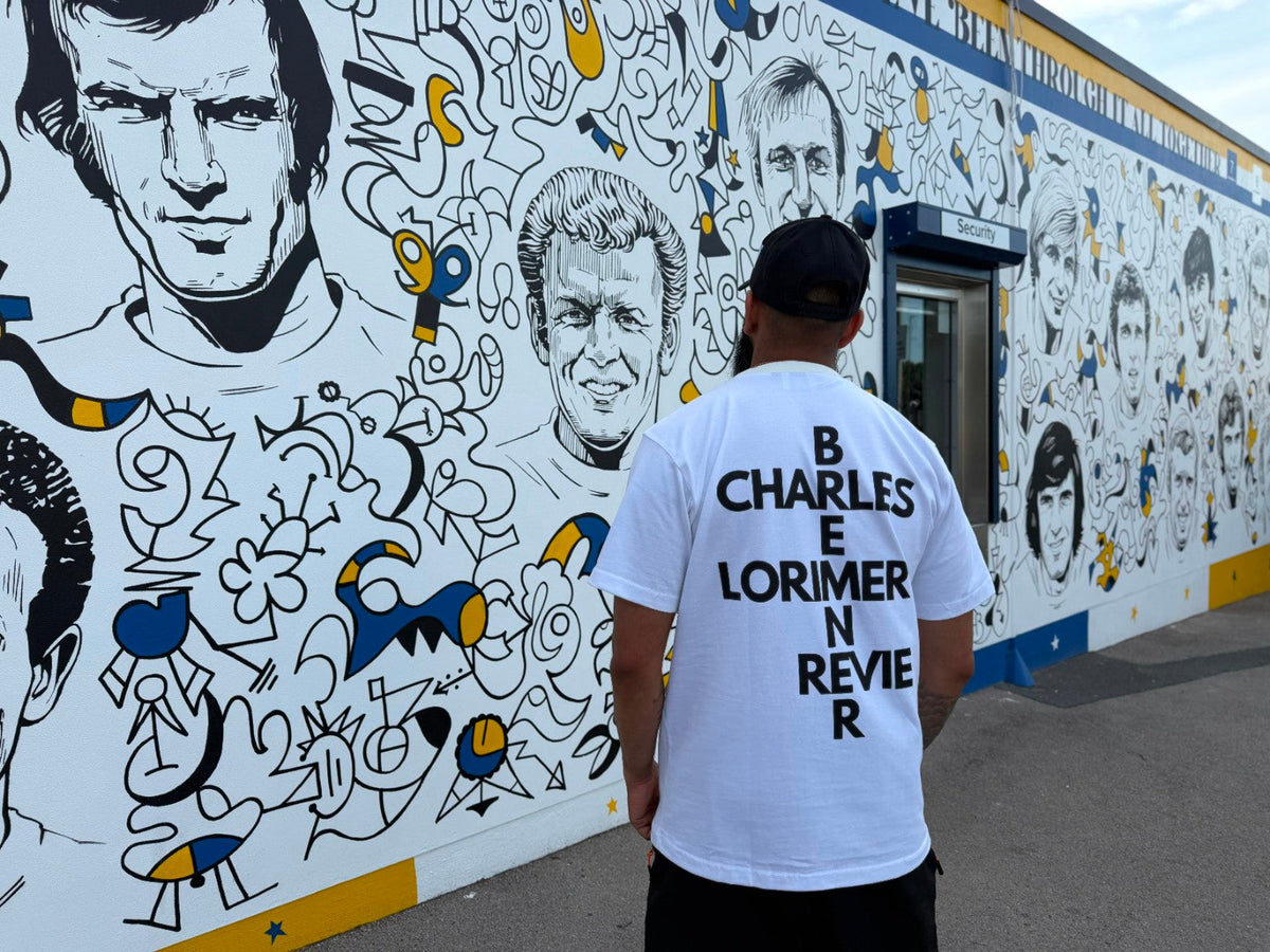 Back of Ananya Garms Bremner & Co white heavyweight T-shirt beside Billy Bremner statue at Elland Road