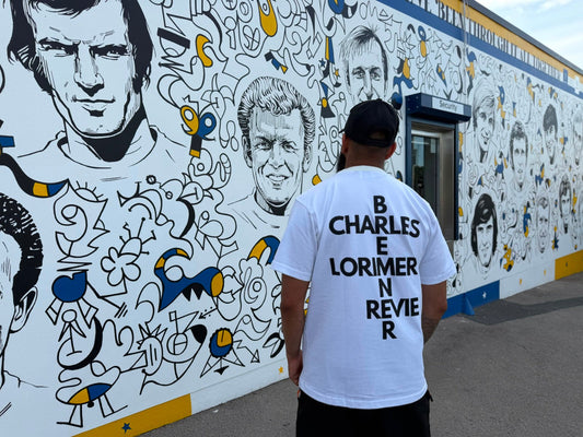 Back of Ananya Garms Bremner & Co white heavyweight T-shirt beside Billy Bremner statue at Elland Road
